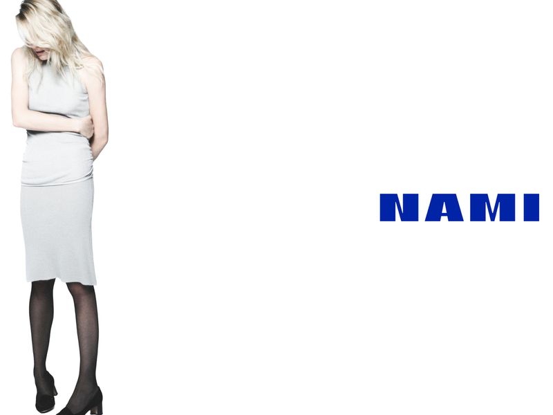 Model Dree Hemingway in a grey dress and black tights standing against a white seamless background with the Nami logo