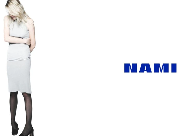 Model Dree Hemingway in a grey dress and black tights standing against a white seamless background with the Nami logo