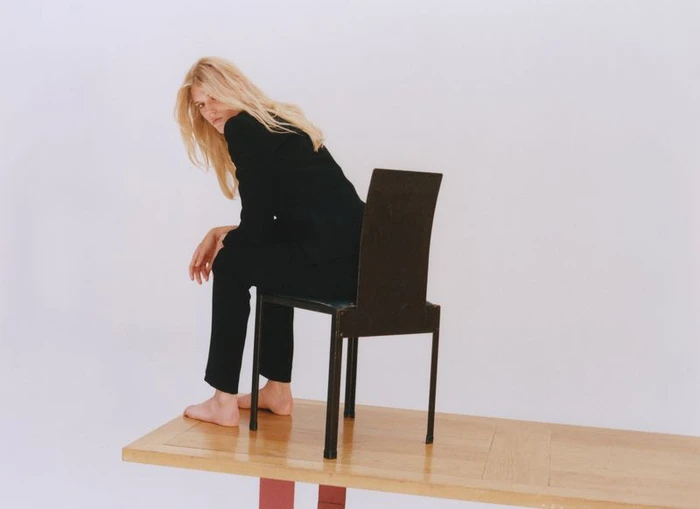 Model Bodine Van Galen seated backwards on a black chair atop a wooden table against a plain white background for D Repubblica.
