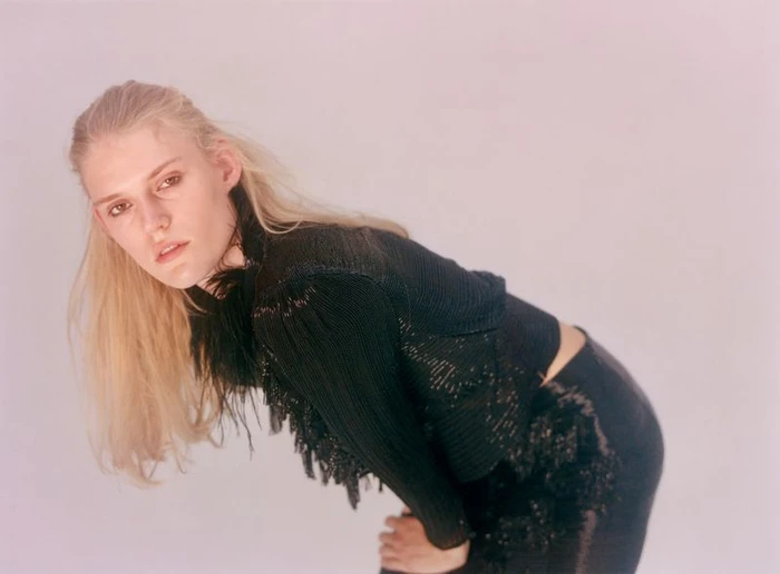 Model Bodine Van Galen wearing a black textured top against a neutral studio background.