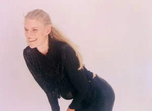Model Bodine Van Galen smiling in a black textured top against a plain light background photographed by Alice Neale.