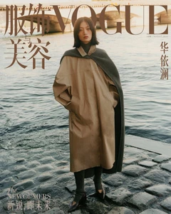 Model standing on stone steps by a river wearing a tan coat and a dark draped knit scarf for Vogue China