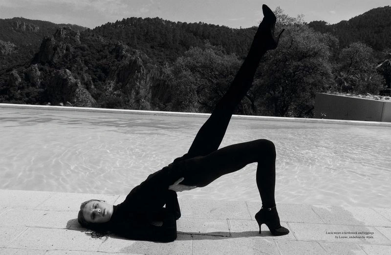 Model performing a bridge stretch in dark clothing by a swimming pool with mountain background