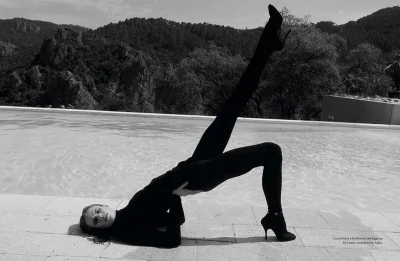 Model performing a bridge stretch in dark clothing by a swimming pool with mountain background