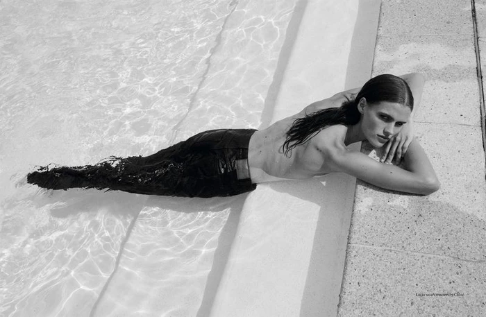 Model lying partially submerged in a swimming pool wearing dark trousers, photographed by Drew Vickers for System Magazine.