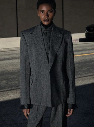 Model in a grey tailored suit jacket standing on a street with a car partially visible in the background.
