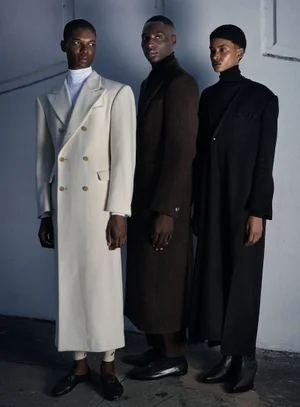 Three models standing side by side wearing long tailored coats against a light wall for Harper's Bazaar Germany.