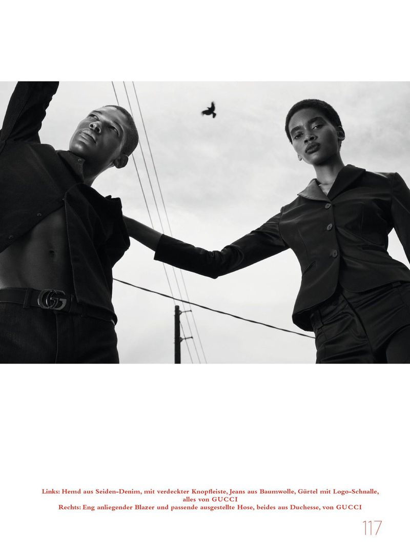 Low-angle black and white fashion editorial featuring a male model and a female model under an overcast sky with a flying bird.