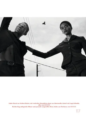 Low-angle black and white fashion editorial featuring a male model and a female model under an overcast sky with a flying bird.