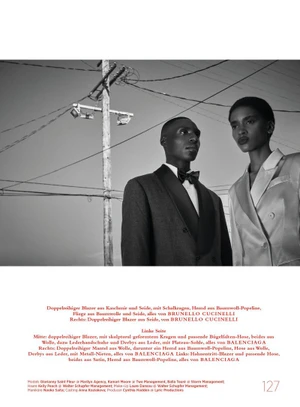 Black and white editorial fashion portrait of a man in a tuxedo and a woman in a tailored suit beneath overhead power lines
