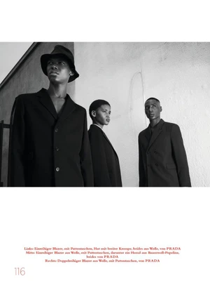 Three models wearing dark tailored blazers against a textured light wall in a black and white editorial photograph.