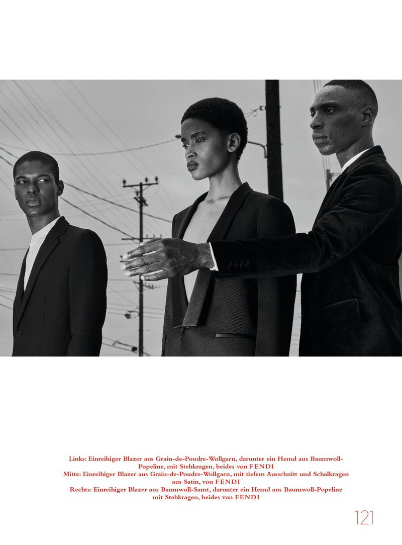 Three models wearing tailored black blazers posing outdoors against a pale sky and utility poles in a black-and-white editorial portrait.