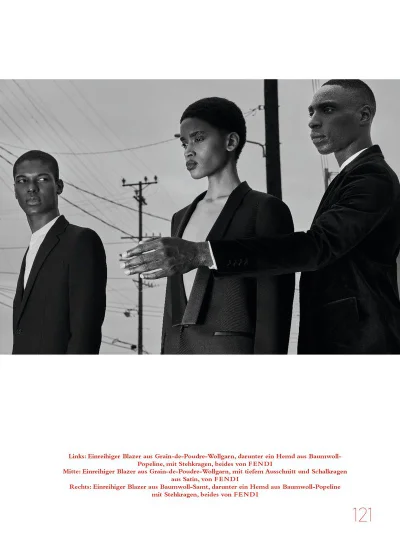 Three models wearing tailored black blazers posing outdoors against a pale sky and utility poles in a black-and-white editorial portrait.
