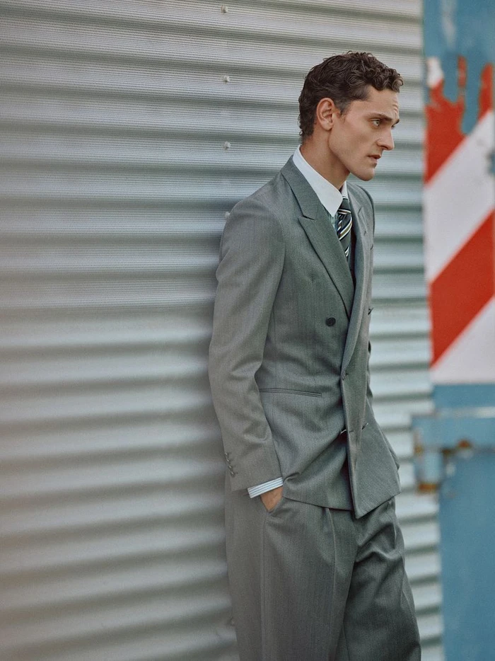 Model Slava Sikorski in a grey double-breasted suit leaning against a corrugated metal wall for Esquire Spain