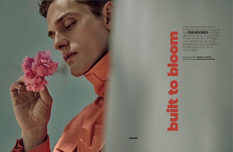 Close-up portrait of a male model in an orange collared jacket holding pink flowers for an Esquire Spain editorial.