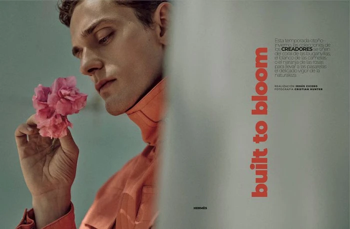 Close-up portrait of a male model in an orange collared jacket holding pink flowers for an Esquire Spain editorial.