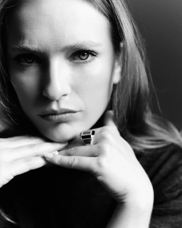 Monochrome portrait of an adult woman with light hair, fair skin, wearing a large ring, resting her chin on her interlaced fingers.