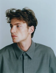 Portrait of Yulef Bopp wearing a slate grey collared shirt against a plain light grey background for The Modern Suit project.