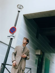 Model Yulef Bopp wearing a beige suit standing next to a street sign and lamppost outdoors