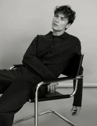 Model Yulef Bopp seated in a chrome armchair wearing a dark collared knit top for The Modern Suit editorial project