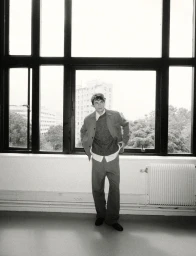 Model standing in a grey suit by large multi-pane windows for The Modern Suit editorial project.