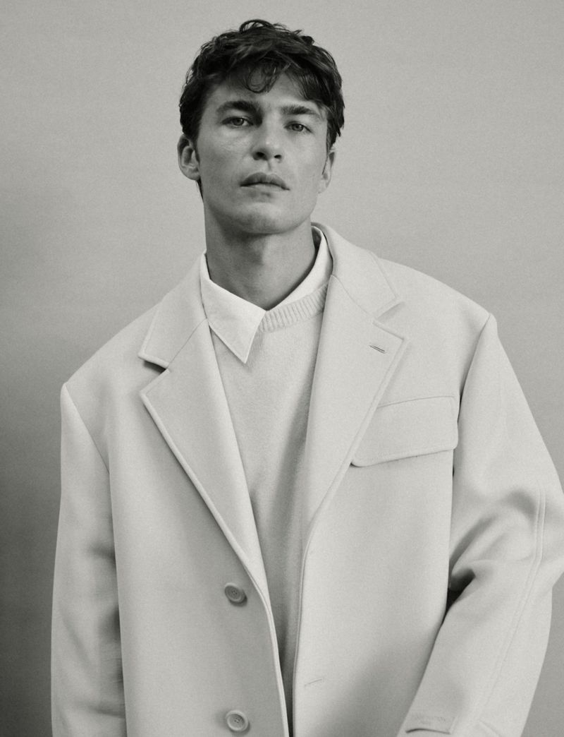 Portrait of model Yulef Bopp wearing an oversized white blazer and layered shirt against a plain studio background