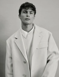 Portrait of model Yulef Bopp wearing an oversized white blazer and layered shirt against a plain studio background
