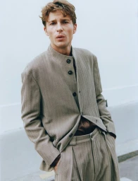 Model Yulef Bopp wearing a textured grey suit jacket and matching trousers against an outdoor wall.
