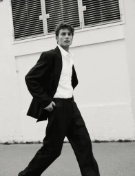 Monochrome image of model Yulef Bopp walking outdoors in a black suit and white shirt for The Modern Suit project.