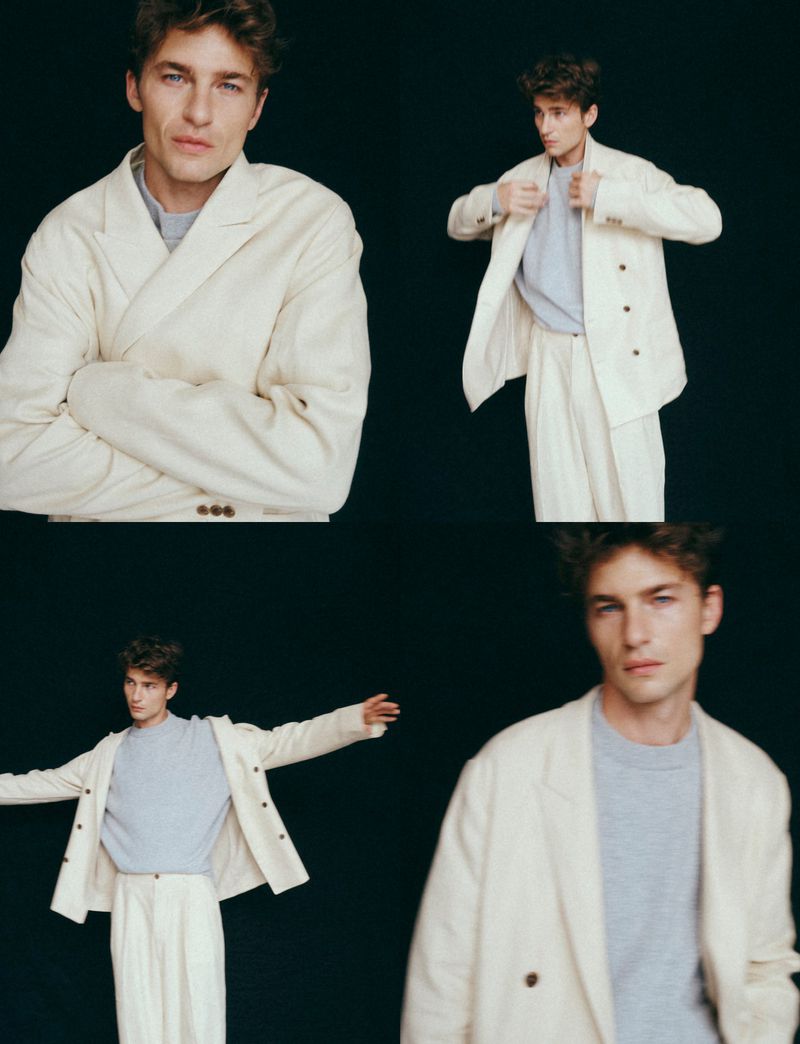 Model Yulef Bopp wearing a cream suit jacket and grey sweater against a solid black background.