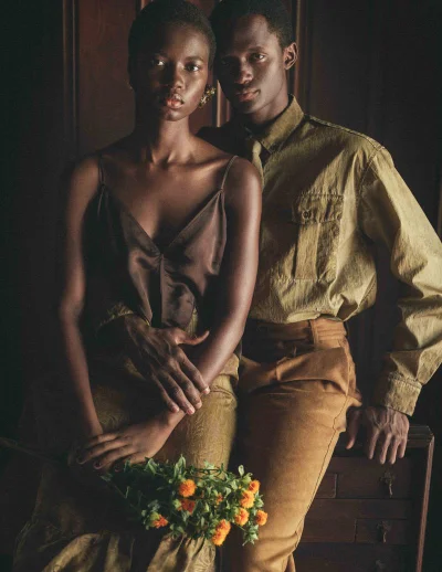 A Black woman and man posing together for L Officiel Italia Fall Escape editorial, holding small yellow flowers.