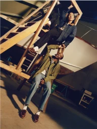 Two models posing on and around a wooden ladder structure wearing jackets and boat shoes