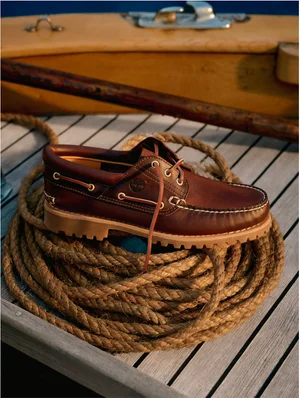Brown leather boat shoe resting on a coil of thick rope on a wooden boat deck