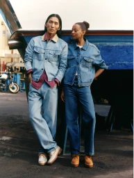 Two models wearing matching denim jackets and boat shoes posing against a blue boat hull.