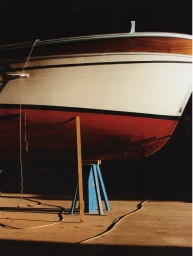 Close-up of the hull of a wooden boat resting on a blue support stand in a dark environment