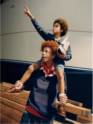 Young person carrying a child on their shoulders holding a model boat in front of a large white hull and wooden planks