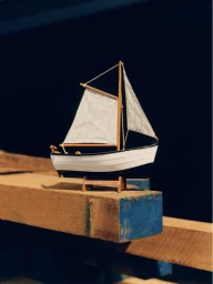 Model sailboat with white sails resting on wooden beams against a dark background for Timberland Boat Shoe 2026.