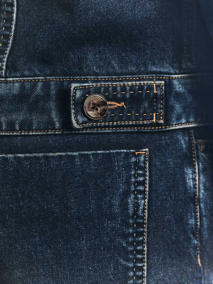 Close-up of dark wash denim jacket with contrast stitching, button tab detail, and a pocket for Louis Vuitton