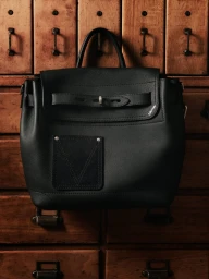 Black leather backpack with a front flap and structured pocket set against a warm wooden cabinet with brass handles.
