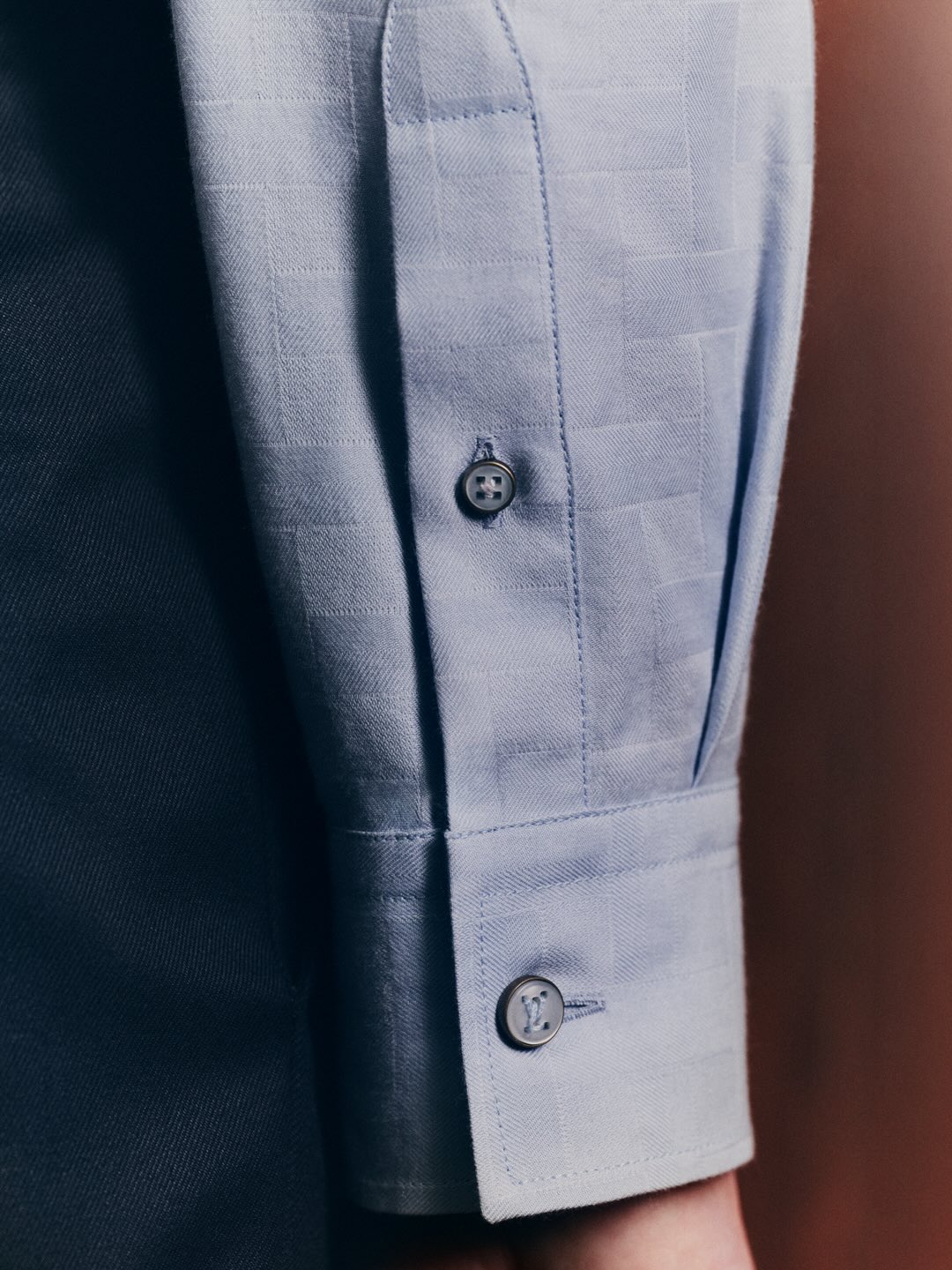 Close-up of a light blue long-sleeved shirt cuff with dark buttons against a dark background