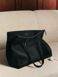 Black leather Louis Vuitton tote bag resting on a light beige upholstered sofa next to a golf ball and tee.