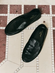 A pair of black leather loafers resting on a patterned mosaic tile floor, shot from above.