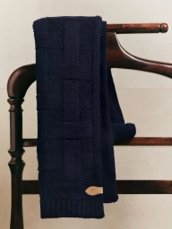 Dark navy blue textured knit scarf draped over a polished dark wood clothes hanger against a neutral background.