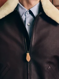 Close-up of a dark brown leather jacket with shearling collar worn over a light blue collared shirt for Louis Vuitton.
