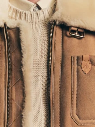 Close-up of a tan suede shearling jacket worn over a textured cream knit sweater by Louis Vuitton.