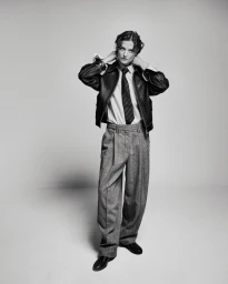 Model in black leather jacket, striped tie, and grey trousers against a grey studio seamless backdrop