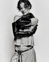 Monochrome portrait of a woman with short wet hair wearing long black leather gloves and a belted outfit against a light background