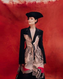 Model in structured black jacket and hat against a textured red painted background for the Louisa project by Ruben Chamorro