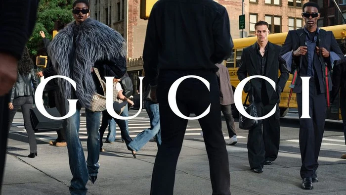 Models in designer fashion walking across a busy city street in front of a yellow bus with bold white Gucci typography overlaid