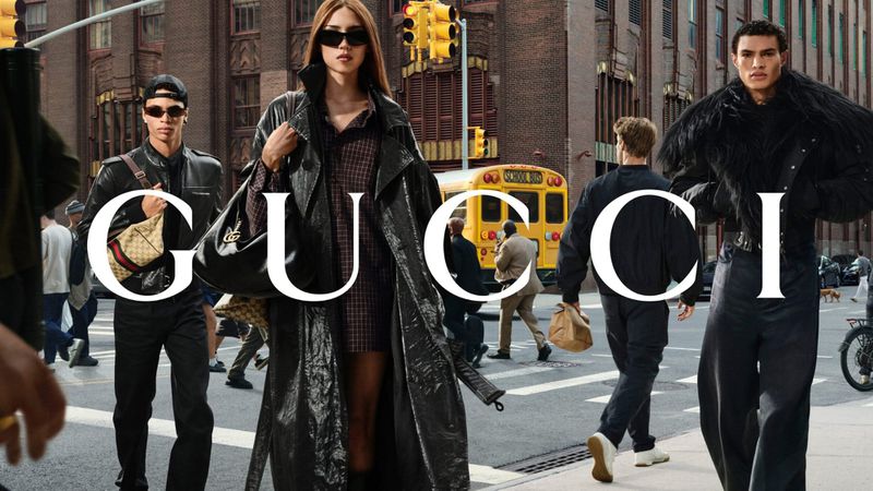 Models in designer outerwear walking on a city street with a yellow school bus in the background